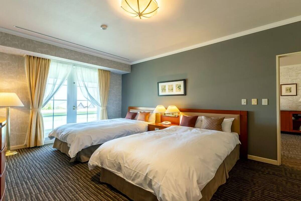 Habitación de hotel con dos camas, un escritorio, una lámpara y vistas a través de la ventana.
