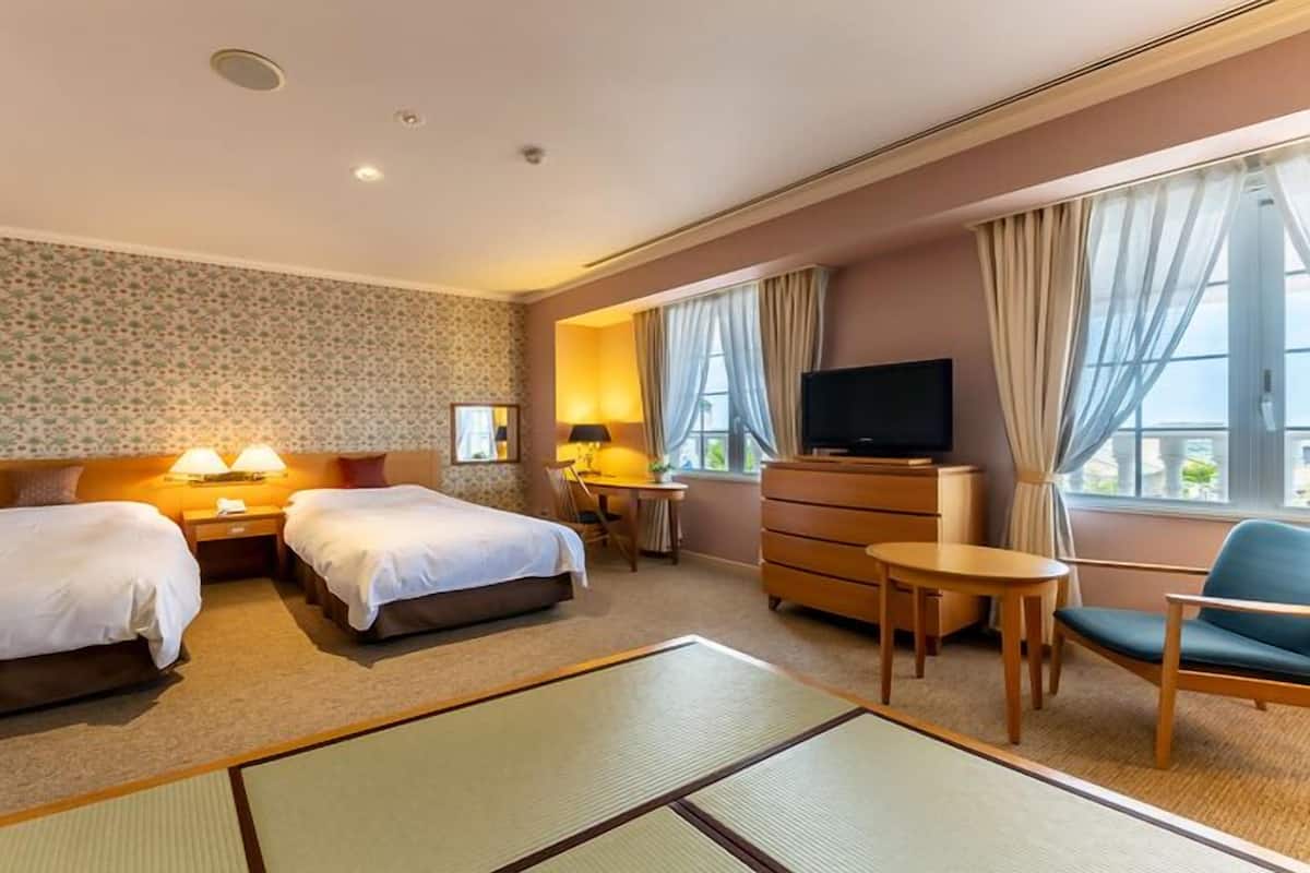 A hotel room with two beds, a TV, a desk, and a chair.