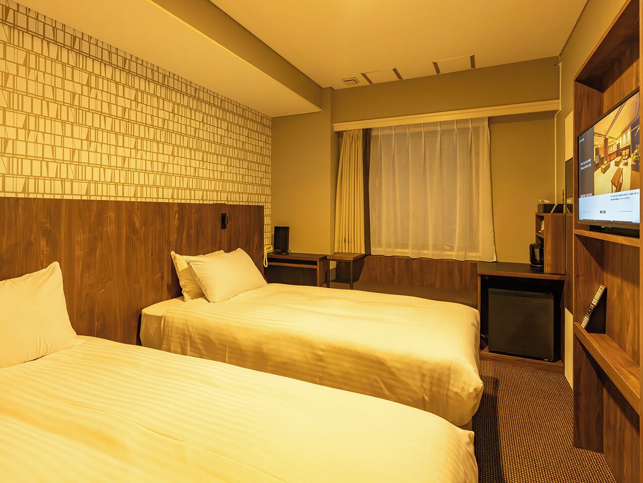 A hotel room with two beds, a television, and a small desk.