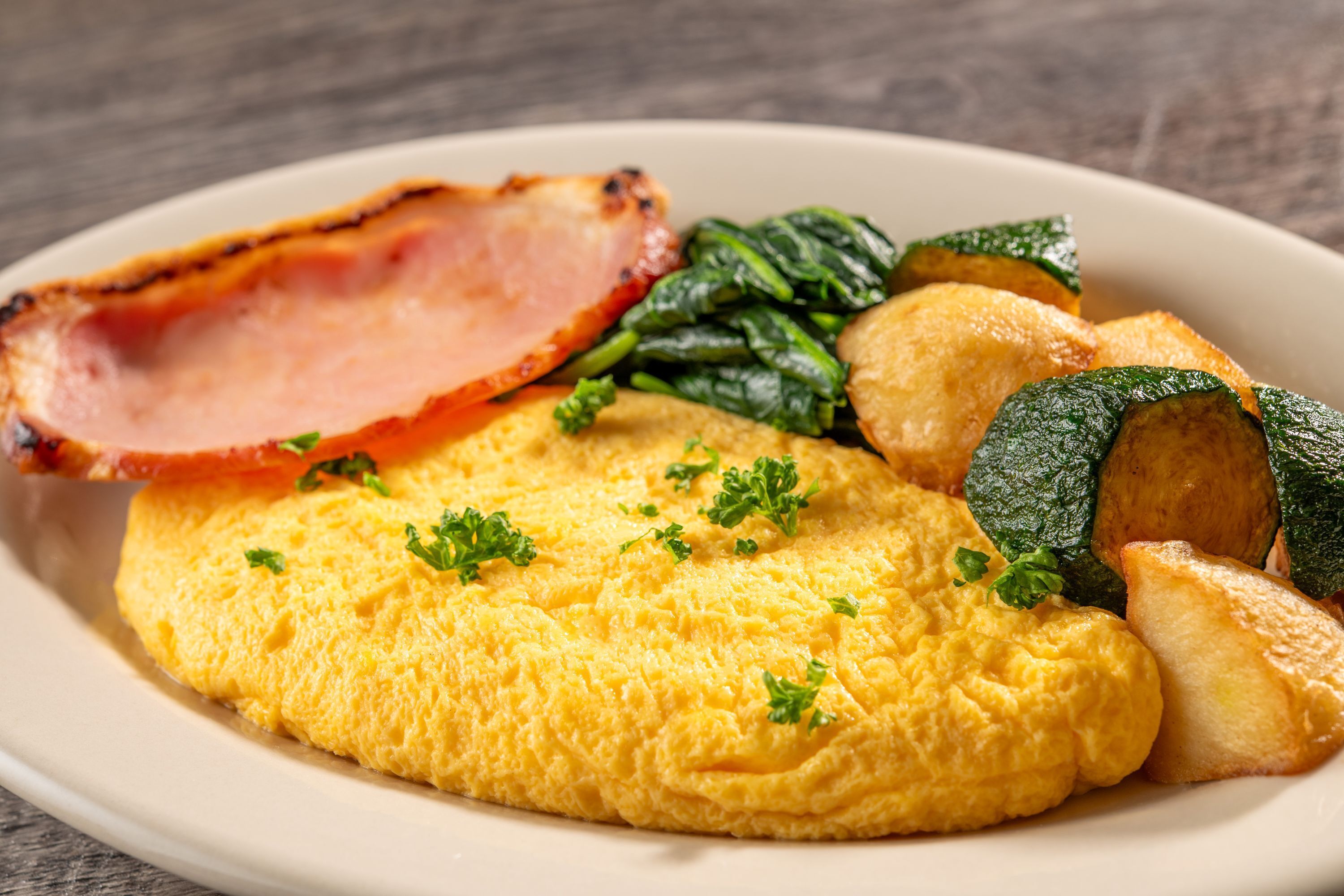 A plate with scrambled eggs, bacon, spinach, and roasted potatoes.