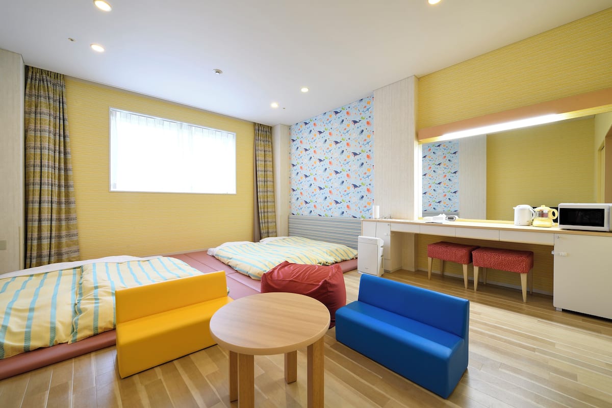A room with a bed, a small table, a blue sofa, a kitchenette, and a window with curtains.