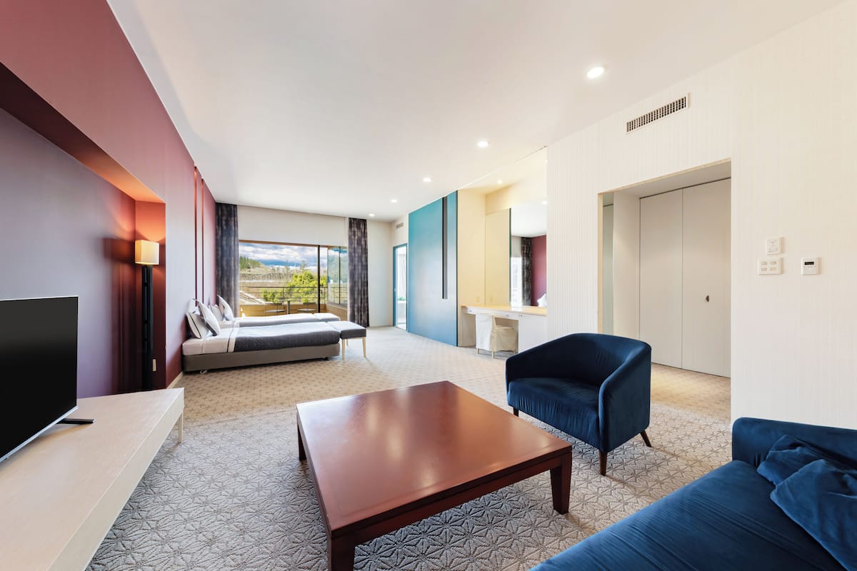 A modern hotel room with a large bed, a sofa, a TV, and a desk area.