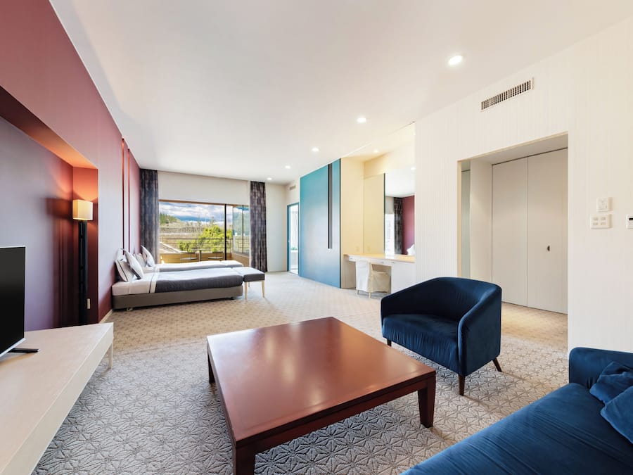 A modern hotel room with a large bed, a sofa, a TV, and a desk area.