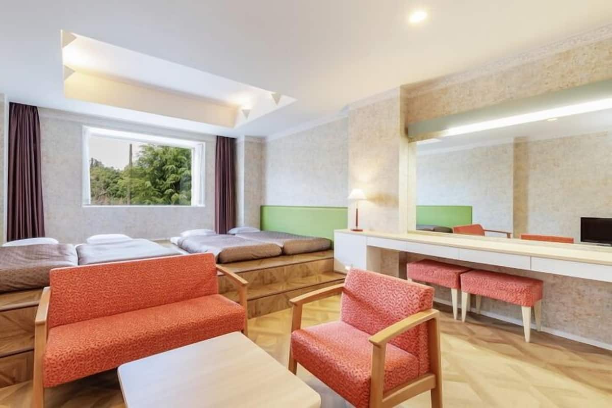 A modern hotel room with a bed, seating area, desk, and a large window.