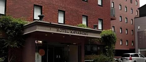A hotel entrance with a brick facade, a sign above the door, and a vehicle parked nearby.