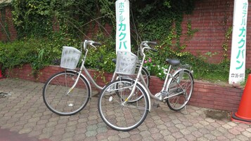 Dos bicicletas estacionadas contra un muro de ladrillo con follaje al fondo.