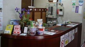 A reception desk with a sign above it, a wall-mounted phone, and various informational posters. - Hotel Kakuban (Yonago)