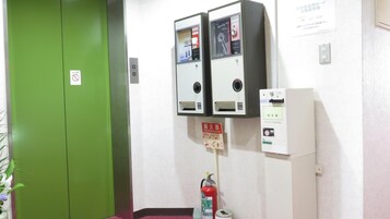 Una habitación con una puerta verde, un extintor y dos máquinas expendedoras en la pared.