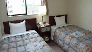 A hotel room with two beds, a nightstand with a lamp, a window with curtains, and a view of the outside. - Hotel Kakuban (Yonago)