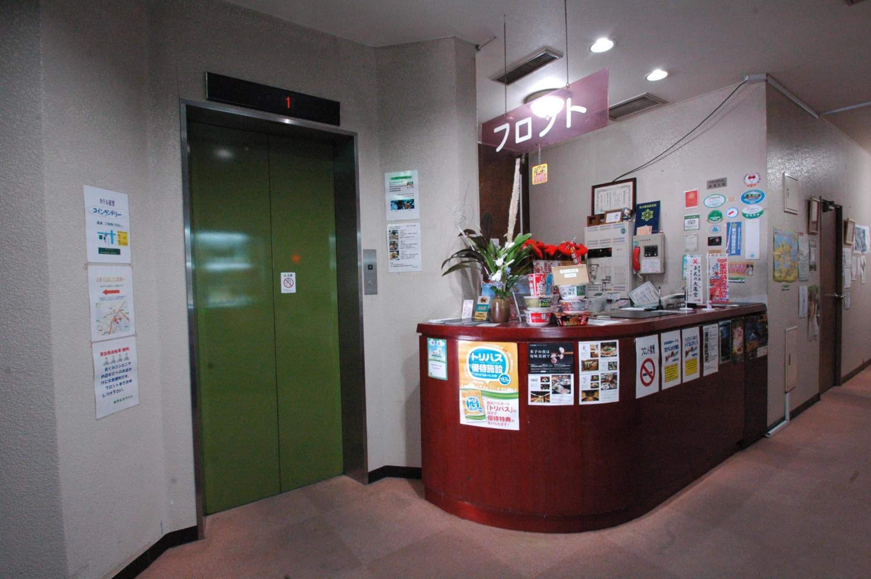 A reception desk with various informational posters, a green elevator, and a sign indicating the floor.