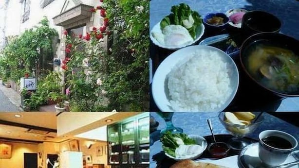 A restaurant with a bar area, a dining table with food, and a view of a building with greenery. - Hotel Kakuban (Yonago)