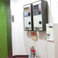 Un extintor montado en una pared con etiqueta roja, un panel de alarma contra incendios y dos máquinas expendedoras.