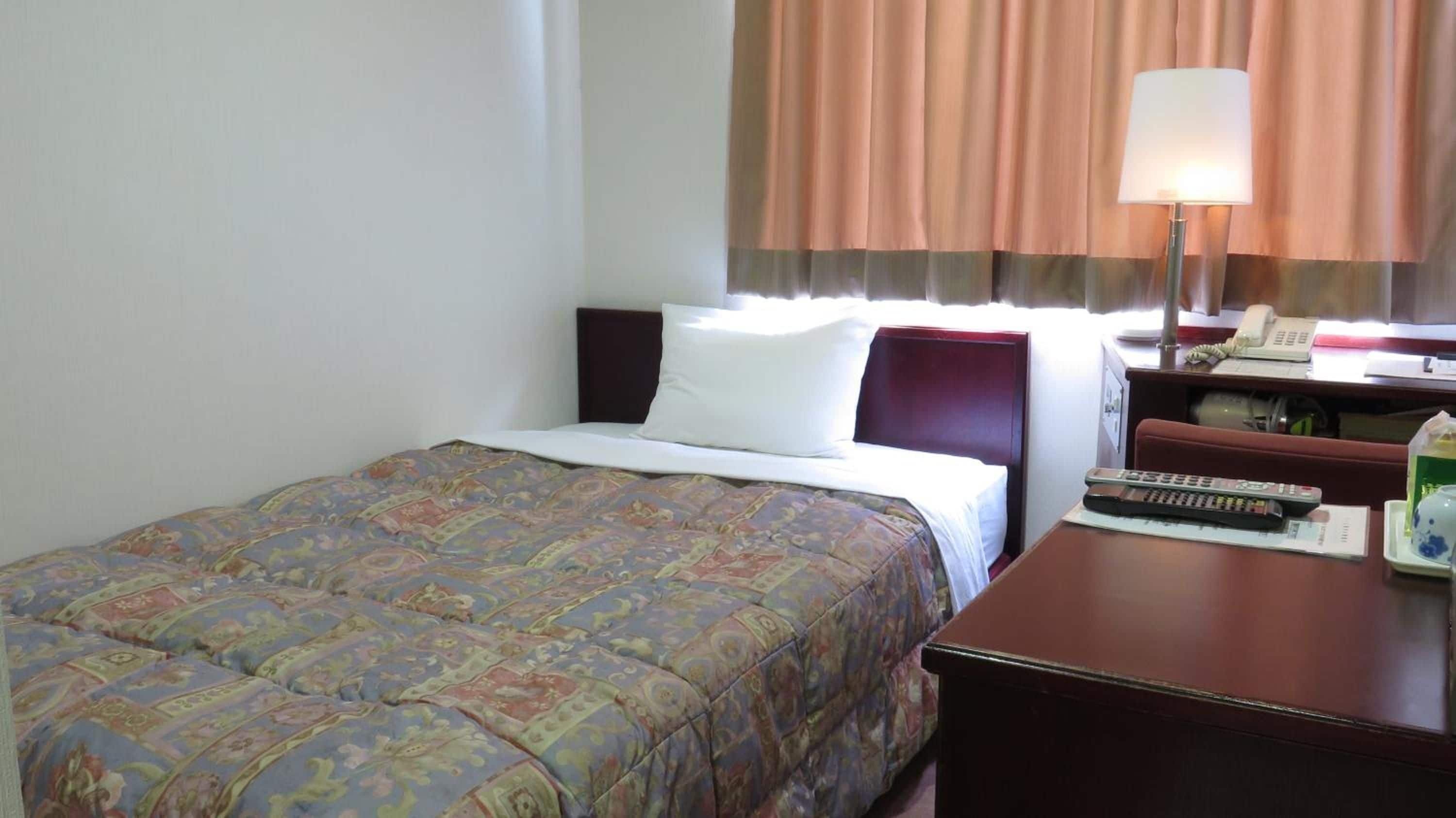 Una habitación de hotel con una cama, un escritorio con una lámpara, un teléfono y un control remoto.