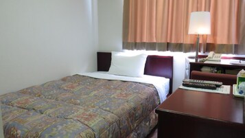 A hotel room with a bed, a desk with a lamp, a telephone, and a remote control.