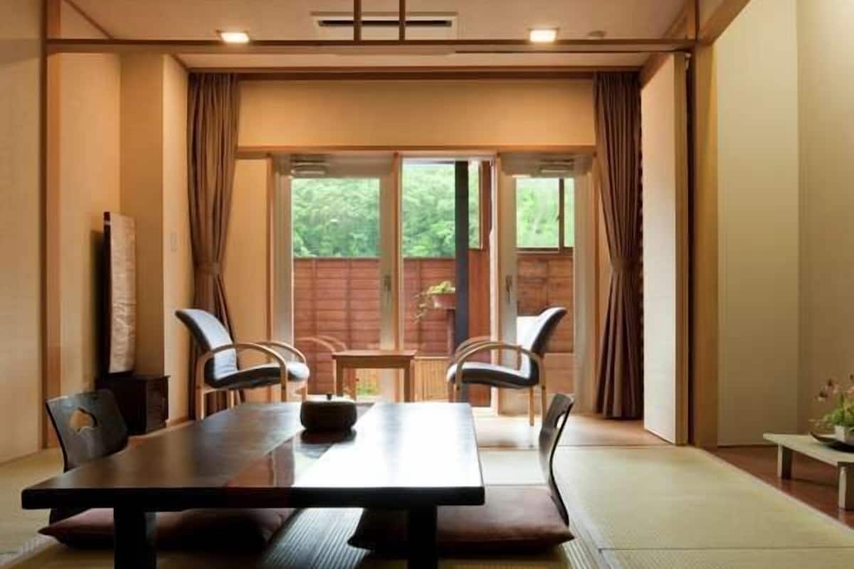 Una habitación con una mesa de madera, cuatro sillas, suelo de tatami y vistas al exterior con vegetación.