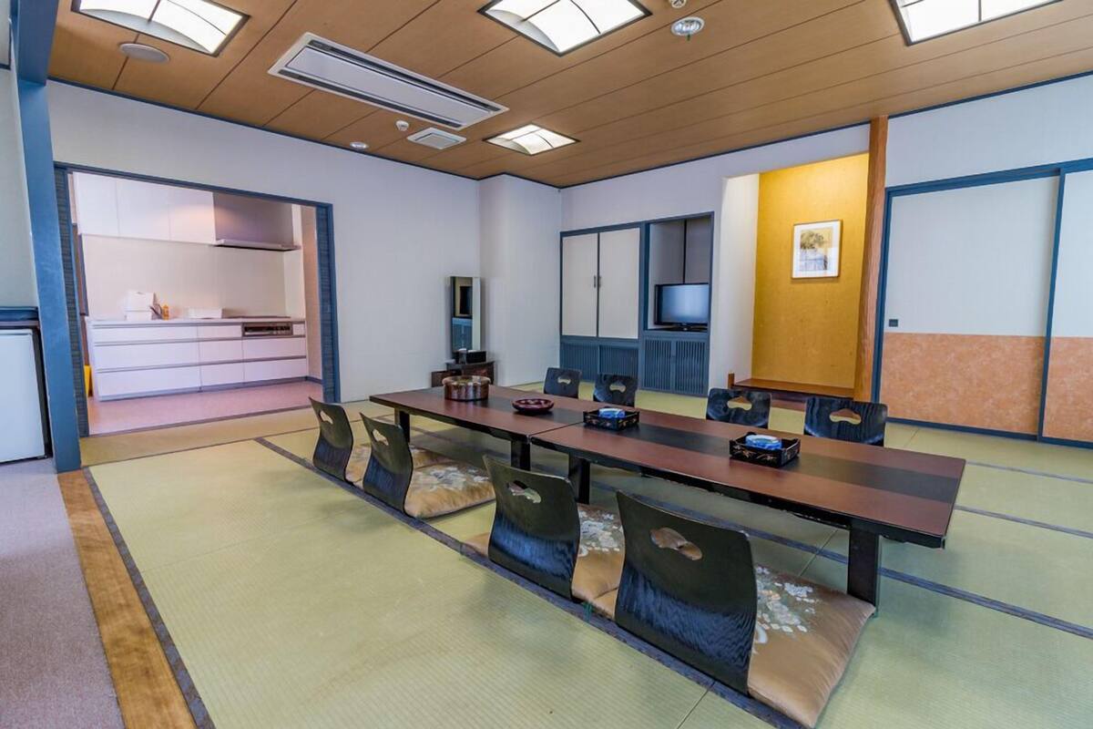 A conference room with a long table, chairs, a television, and a kitchen area in the background.