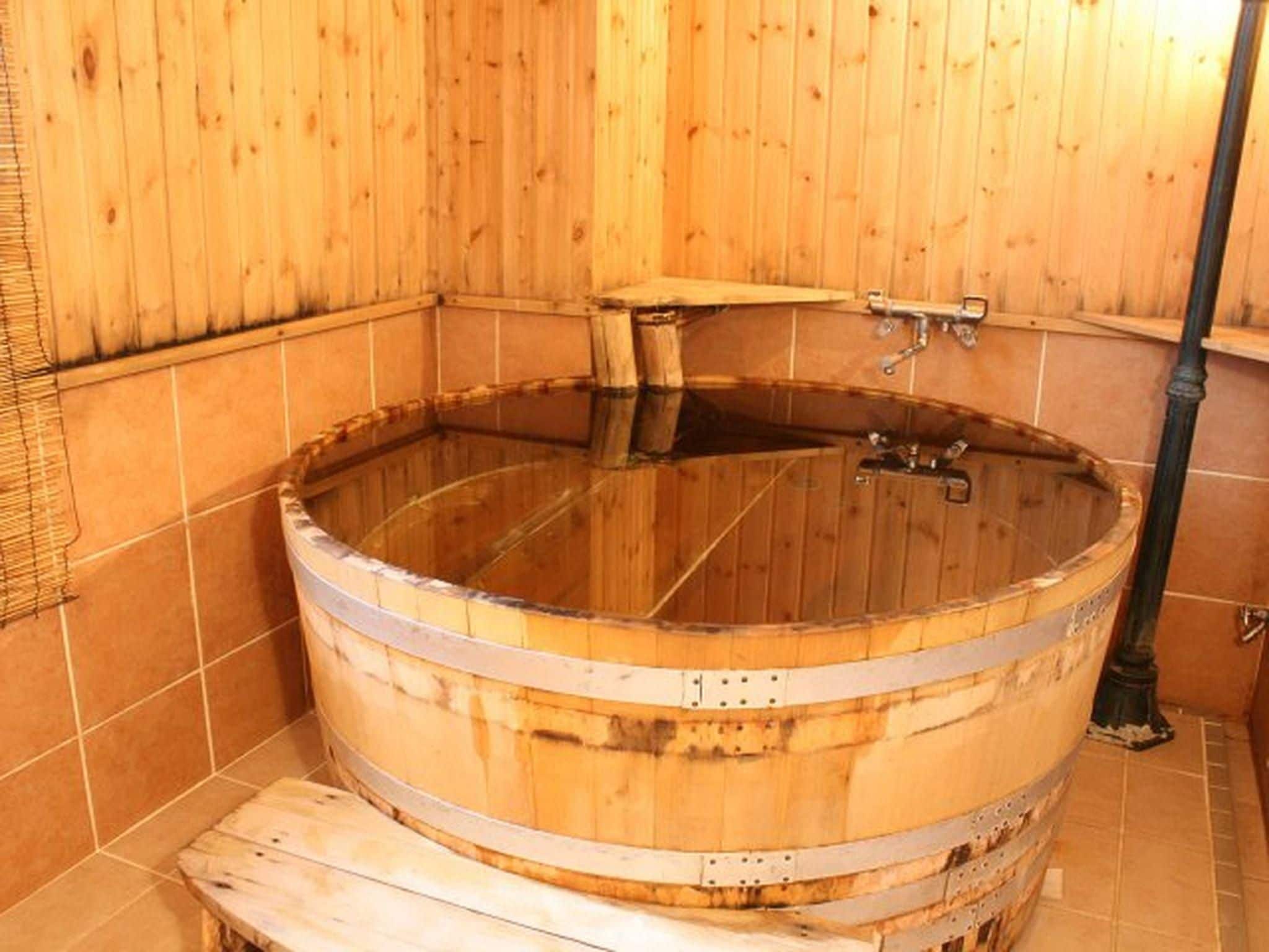 A wooden hot tub with metal fixtures, a wooden bench, and tiled walls.