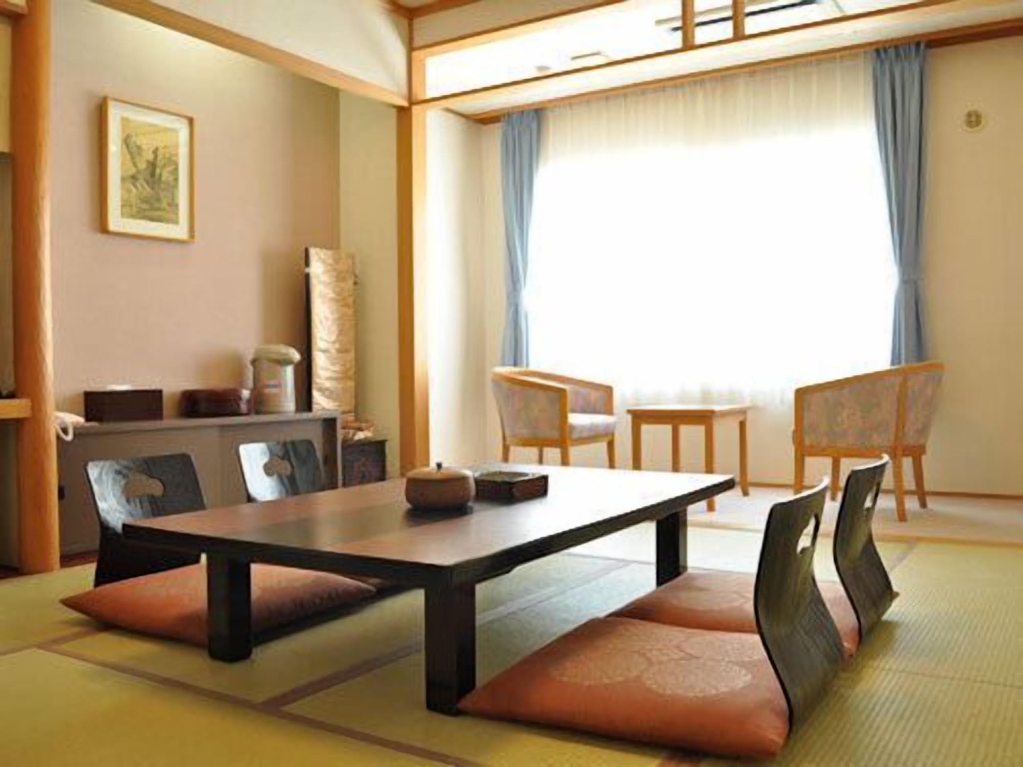 Ein traditioneller japanischer Raum mit Tatami-Bodenbelag, einem niedrigen Tisch, gepolsterten Sitzgelegenheiten und Blick durch einen Shoji-Bildschirm.