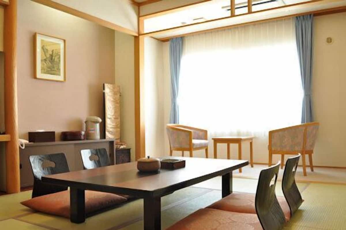 Una habitación japonesa tradicional con suelo de tatami, una mesa baja, asientos acolchados y vistas a través de un shoji.