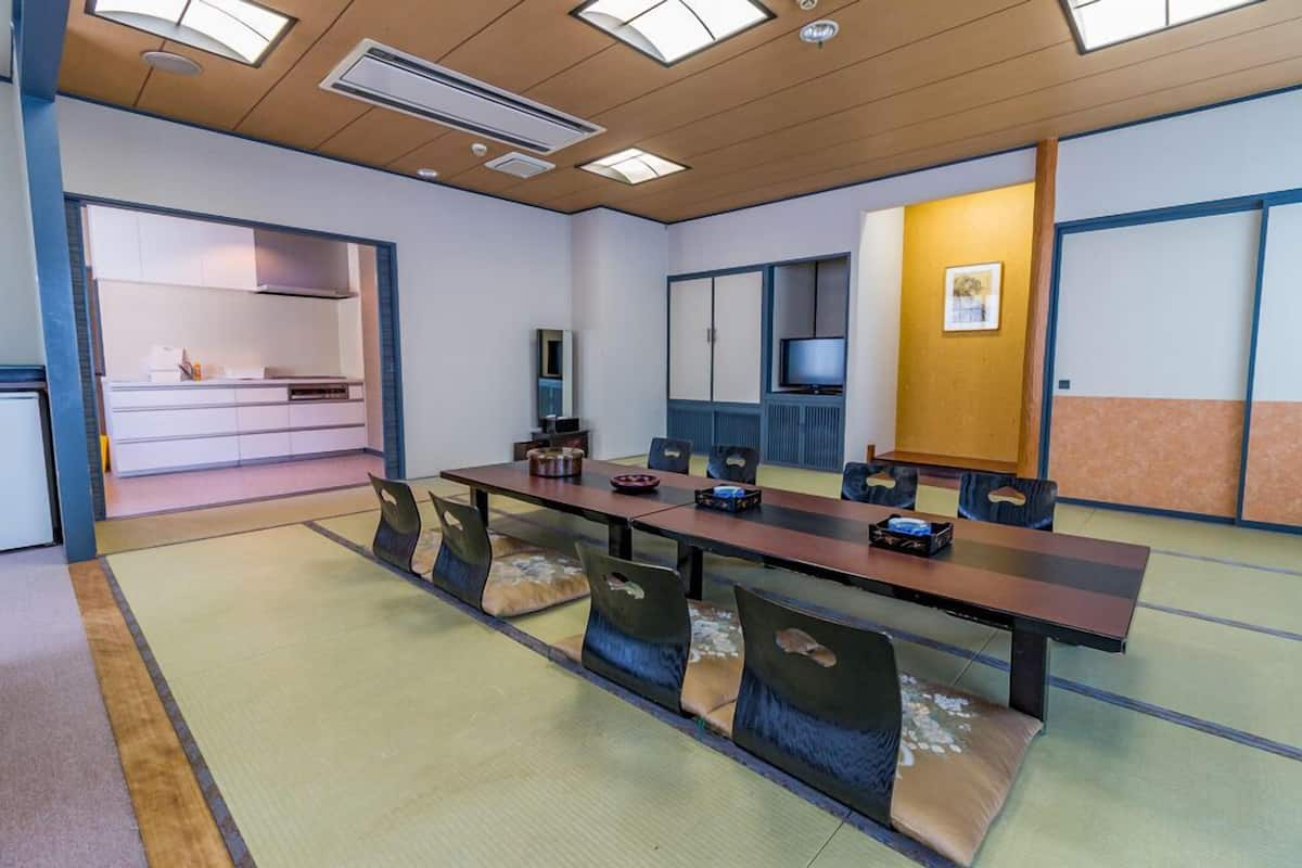 A conference room with a long table, chairs, a television, and a kitchen area in the background.