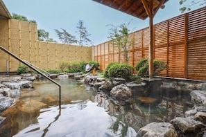 A traditional Japanese onsen with a wooden fence, a stone hot spring, and a wooden walkway. - Hotel Sakushu Musashi (Mimasaka)