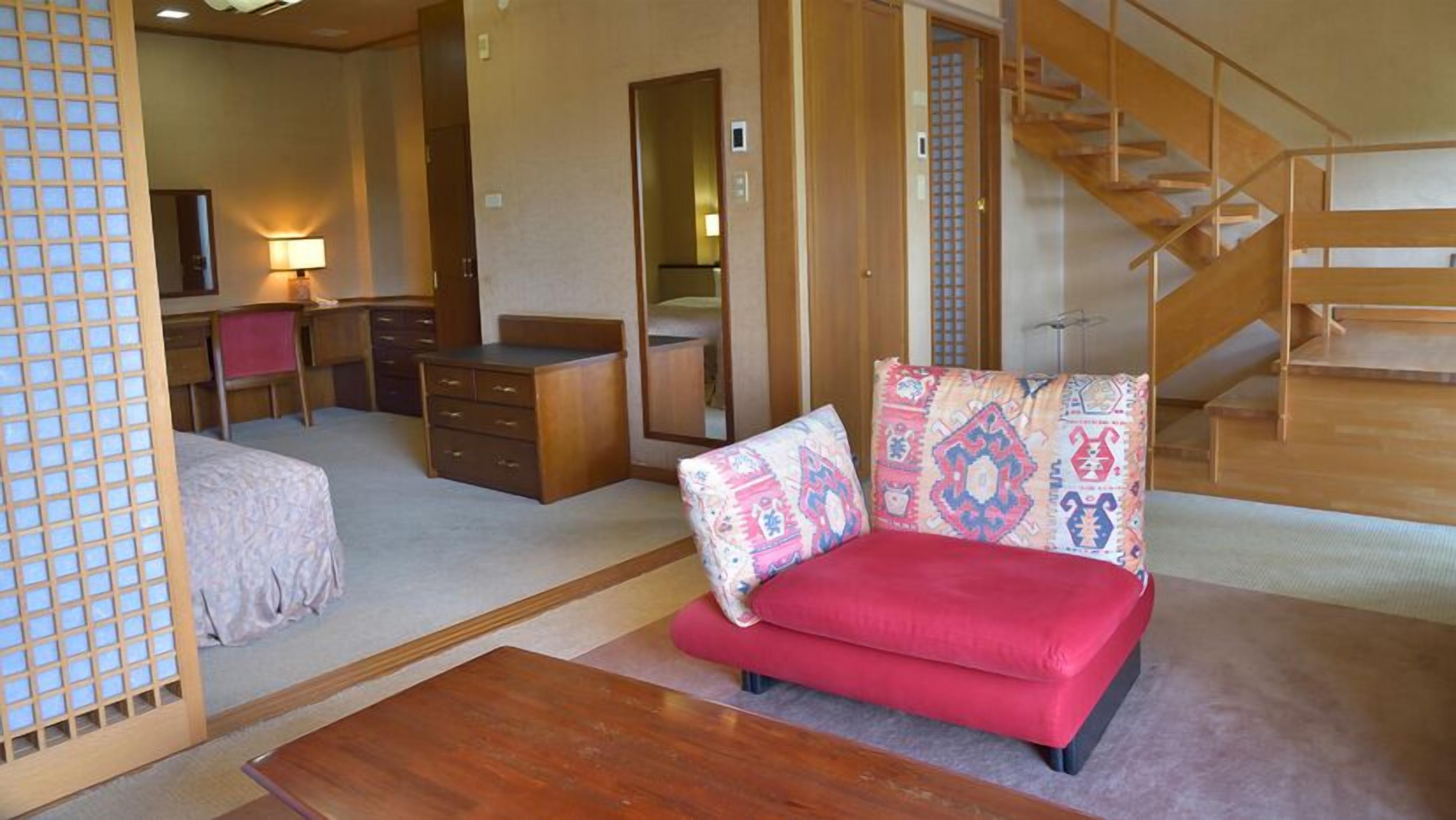 A traditional Japanese-style room with tatami flooring, a low wooden desk, a red sofa, and a wooden staircase.