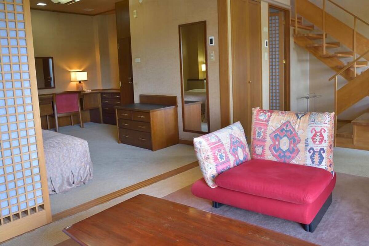 A traditional Japanese-style room with tatami flooring, a low wooden desk, a red sofa, and a wooden staircase.