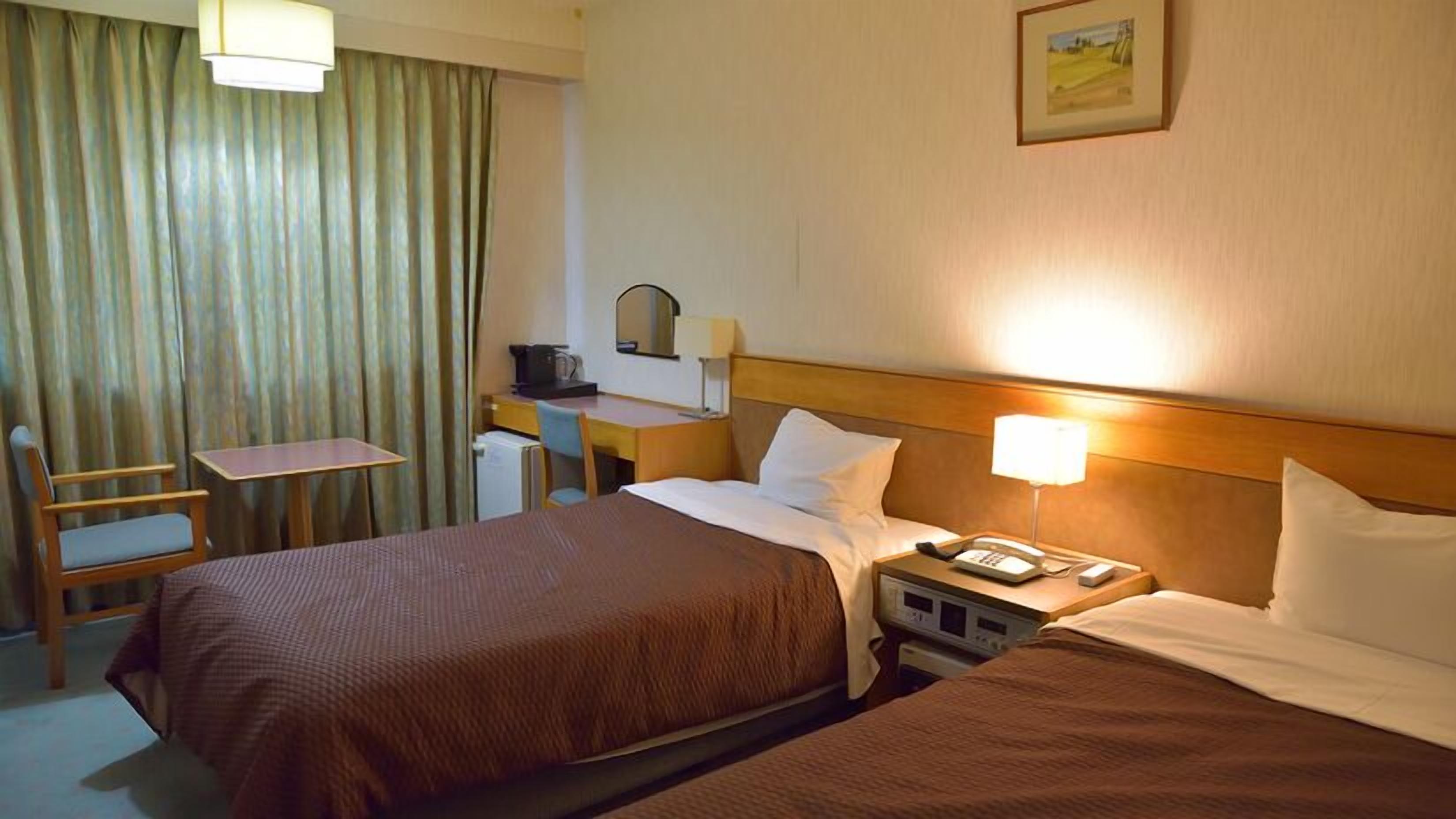 A hotel room with two beds, a desk, a chair, a telephone, and a painting on the wall.