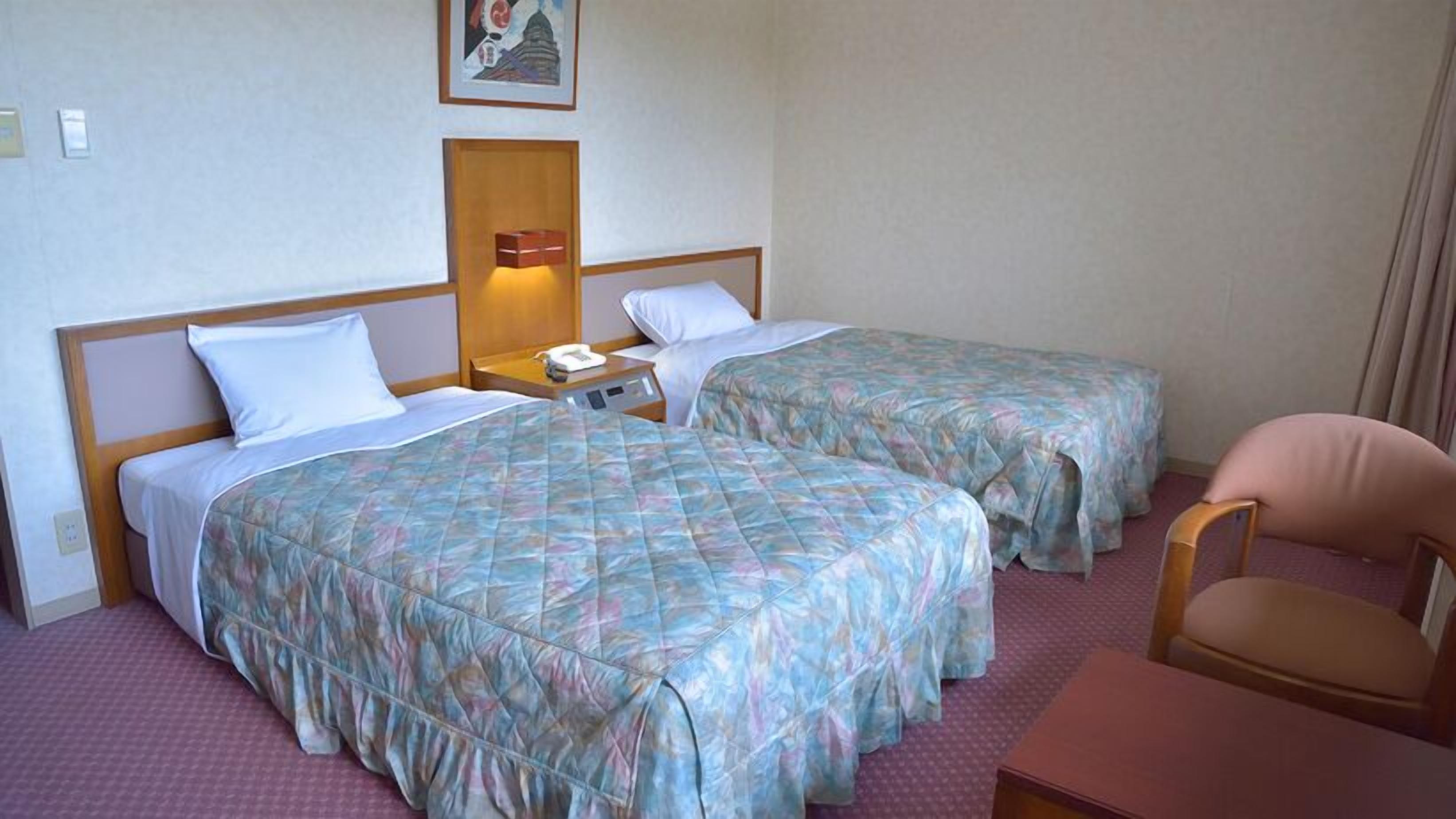 A hotel room with two beds, a nightstand with a lamp, a chair, and a picture on the wall.