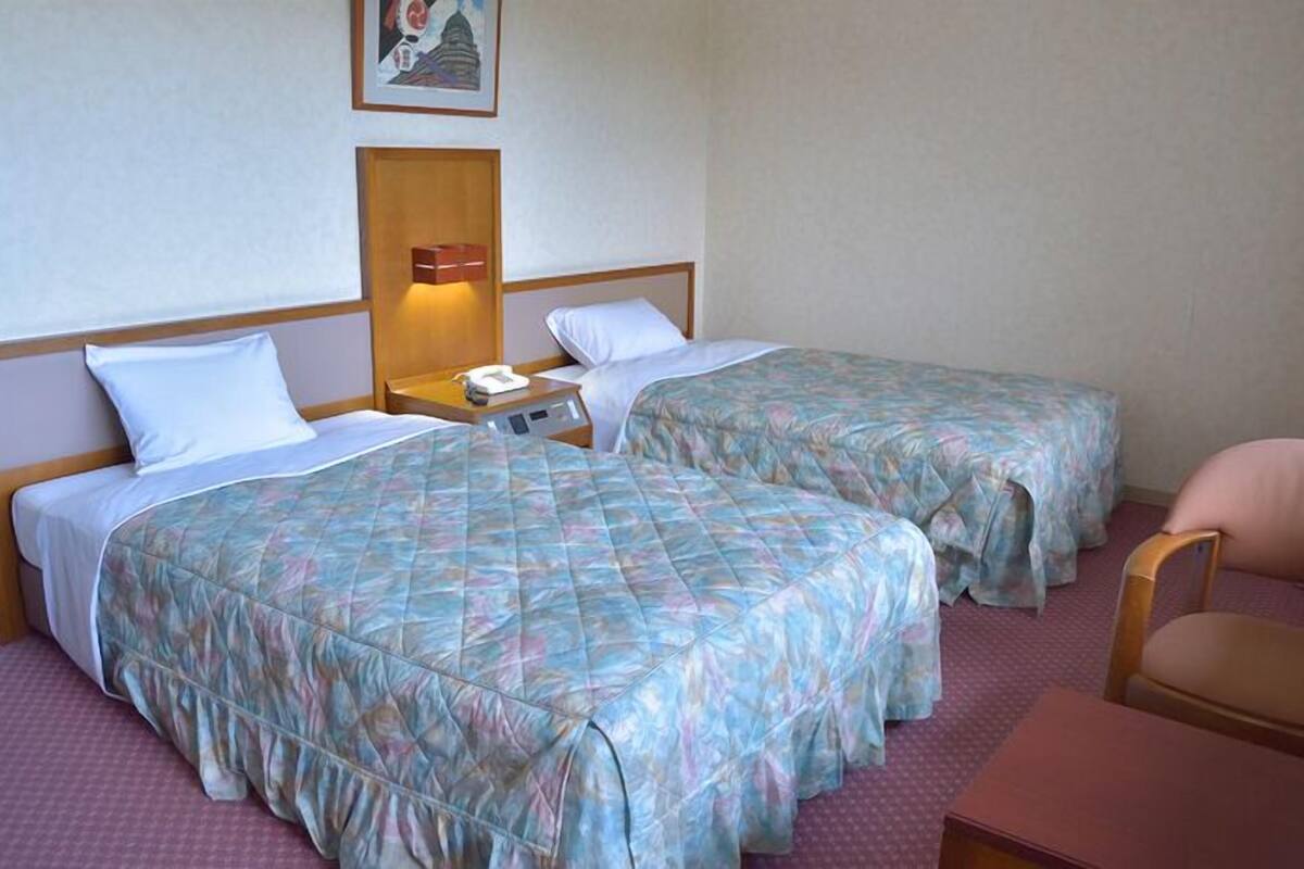 A hotel room with two beds, a nightstand with a lamp, a chair, and a picture on the wall.