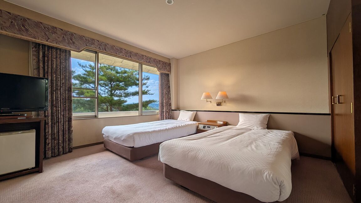 A hotel room with two beds, a TV, a desk, and a window with a view.