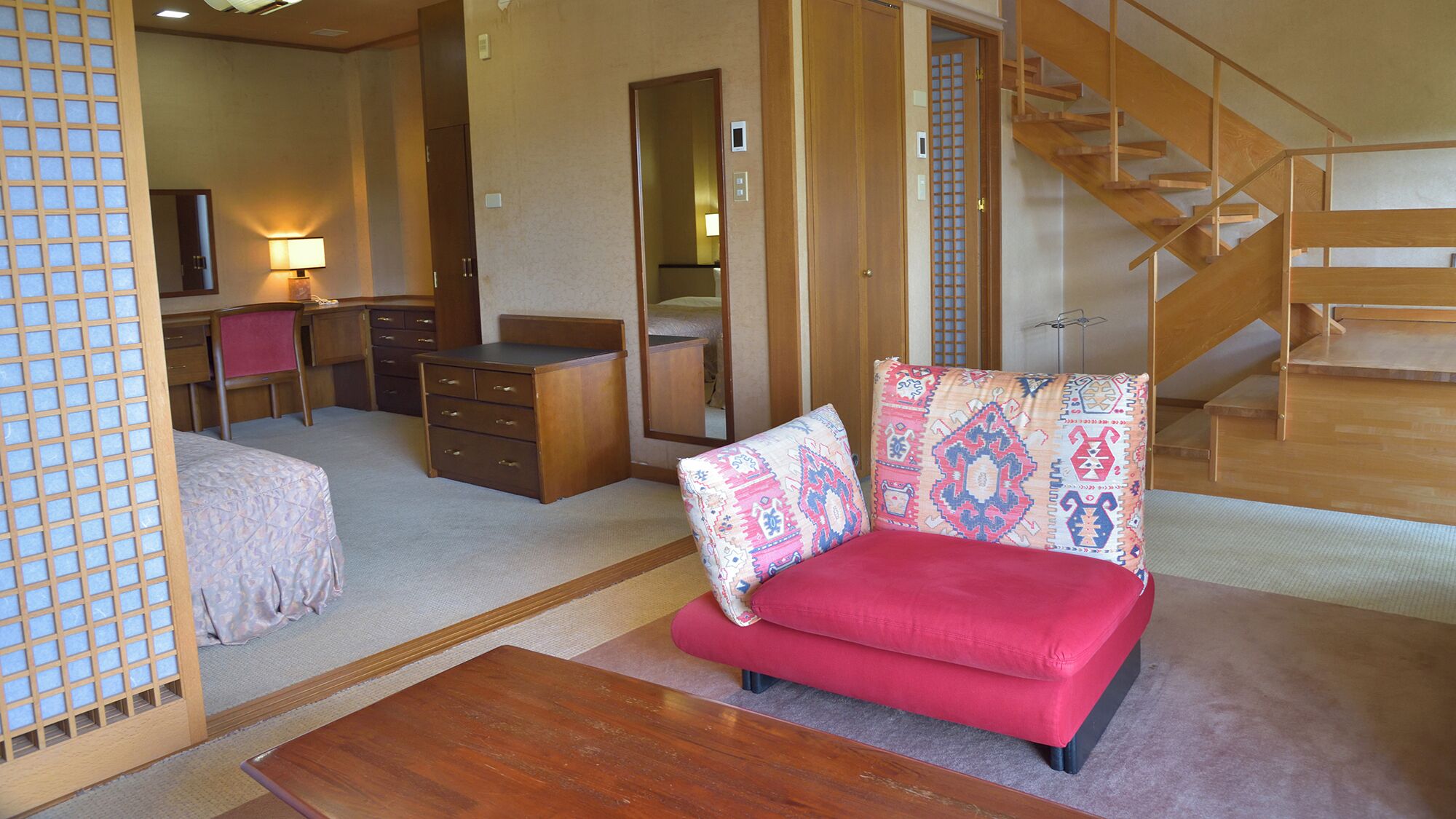 A traditional Japanese-style room with tatami flooring, a low wooden desk, a red sofa, and a wooden staircase.