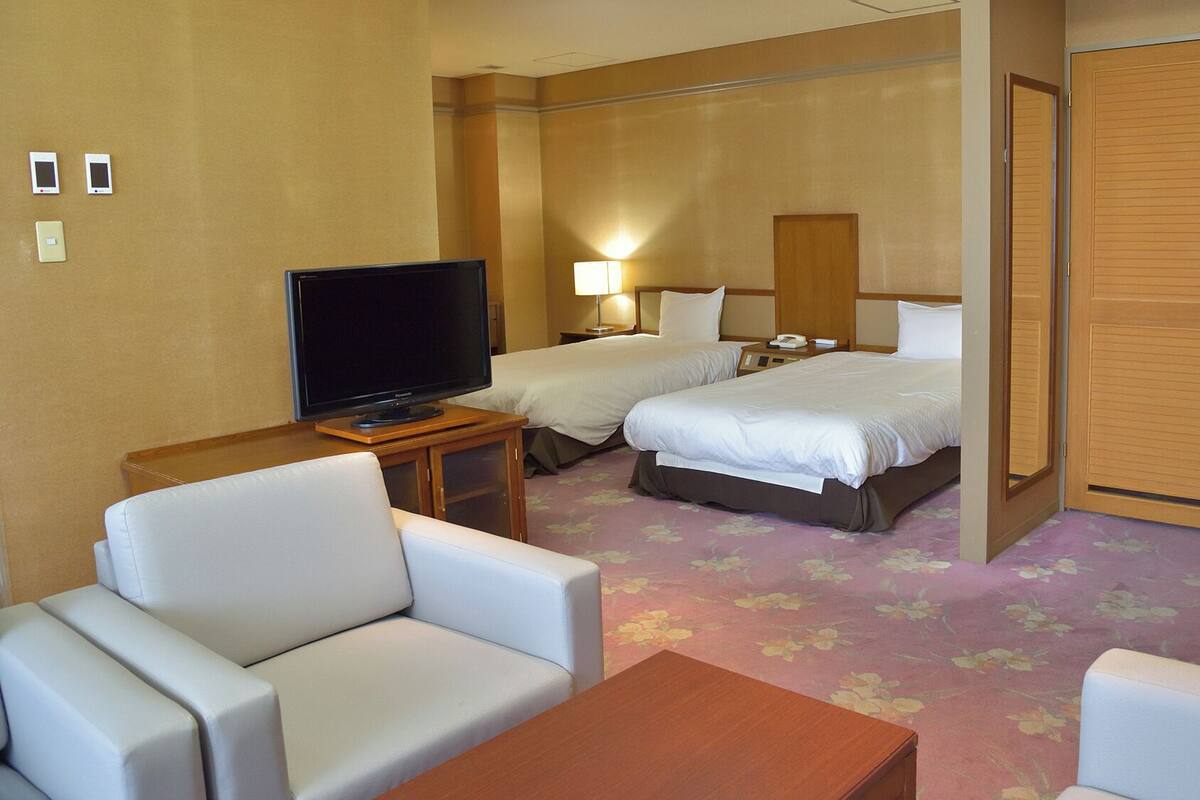 A hotel room with a television, two beds, a desk, and a seating area.