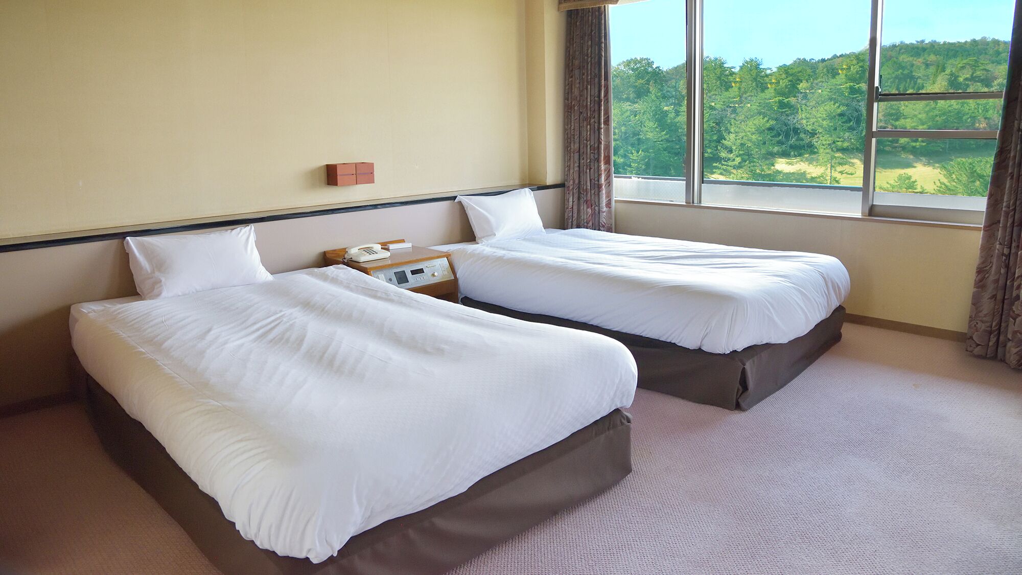 A hotel room with two beds, a bedside phone, and a window with a view of a forest.