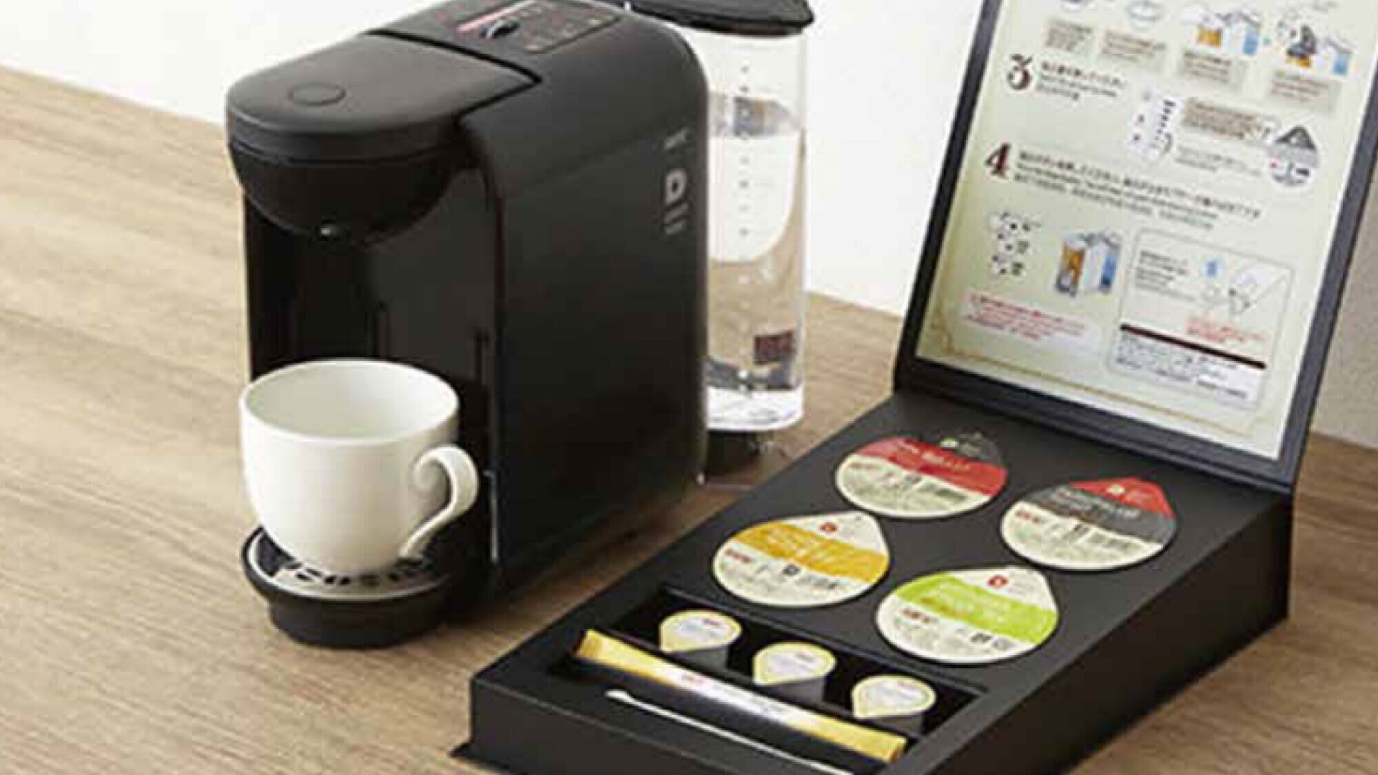 A coffee maker with a cup, a glass of water, and a booklet with coffee pods.