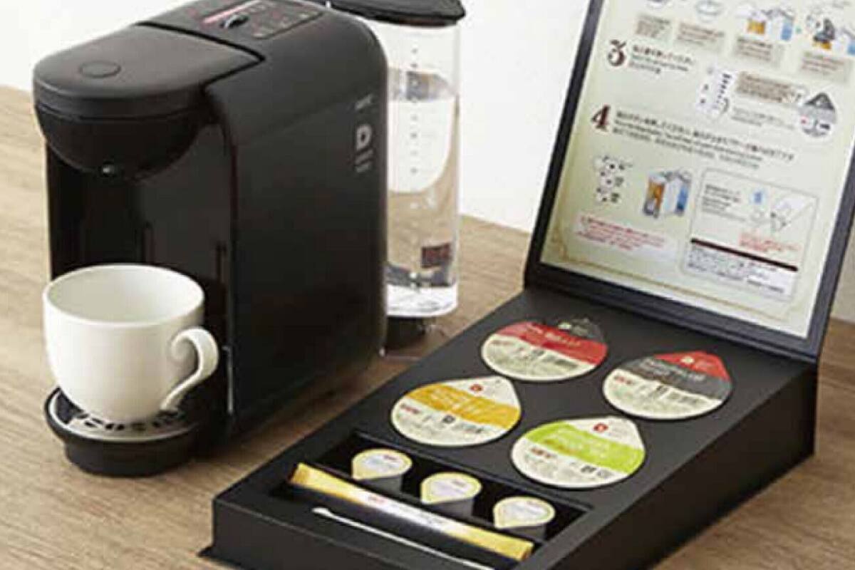 A coffee maker with a cup, a glass of water, and a booklet with coffee pods.