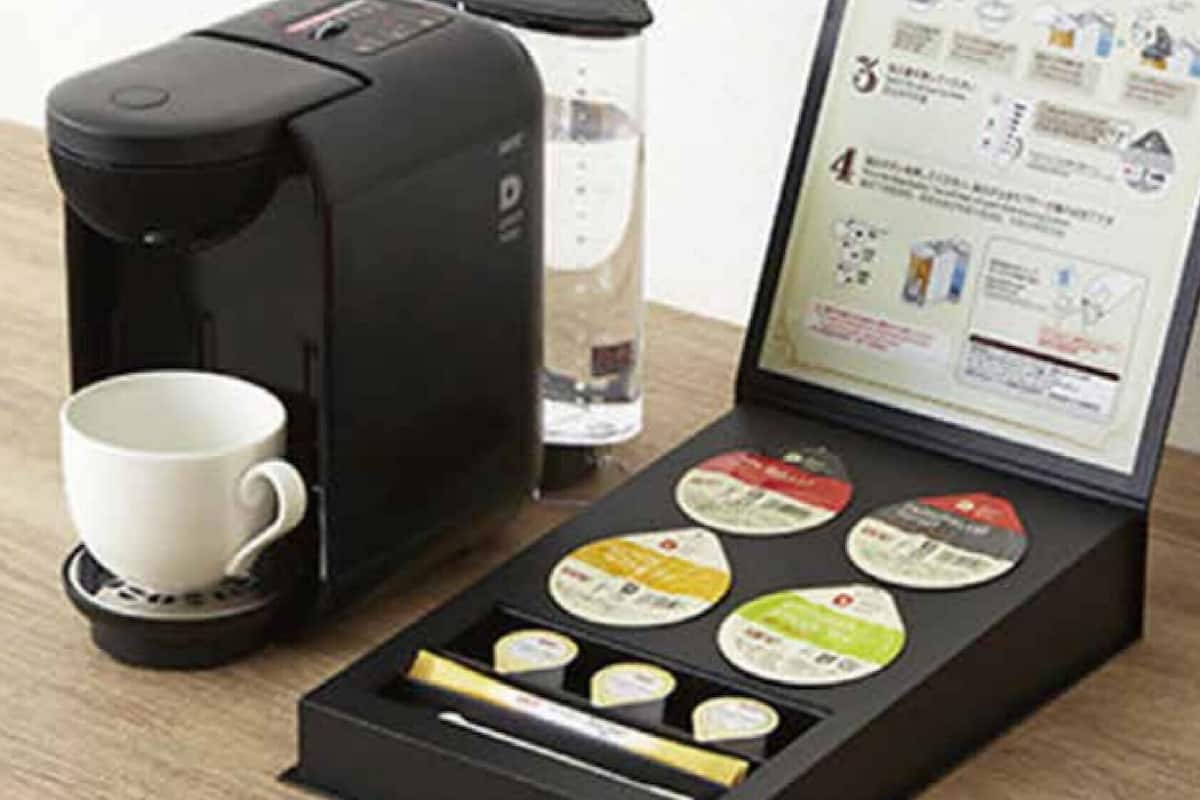 A coffee maker with a cup, a glass of water, and a booklet with coffee pods.