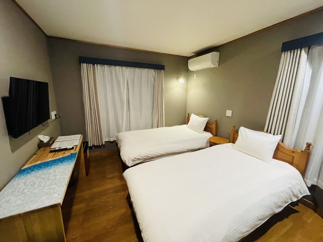 A hotel room with two beds, a desk with a laptop, a flat-screen TV, and an air conditioning unit.