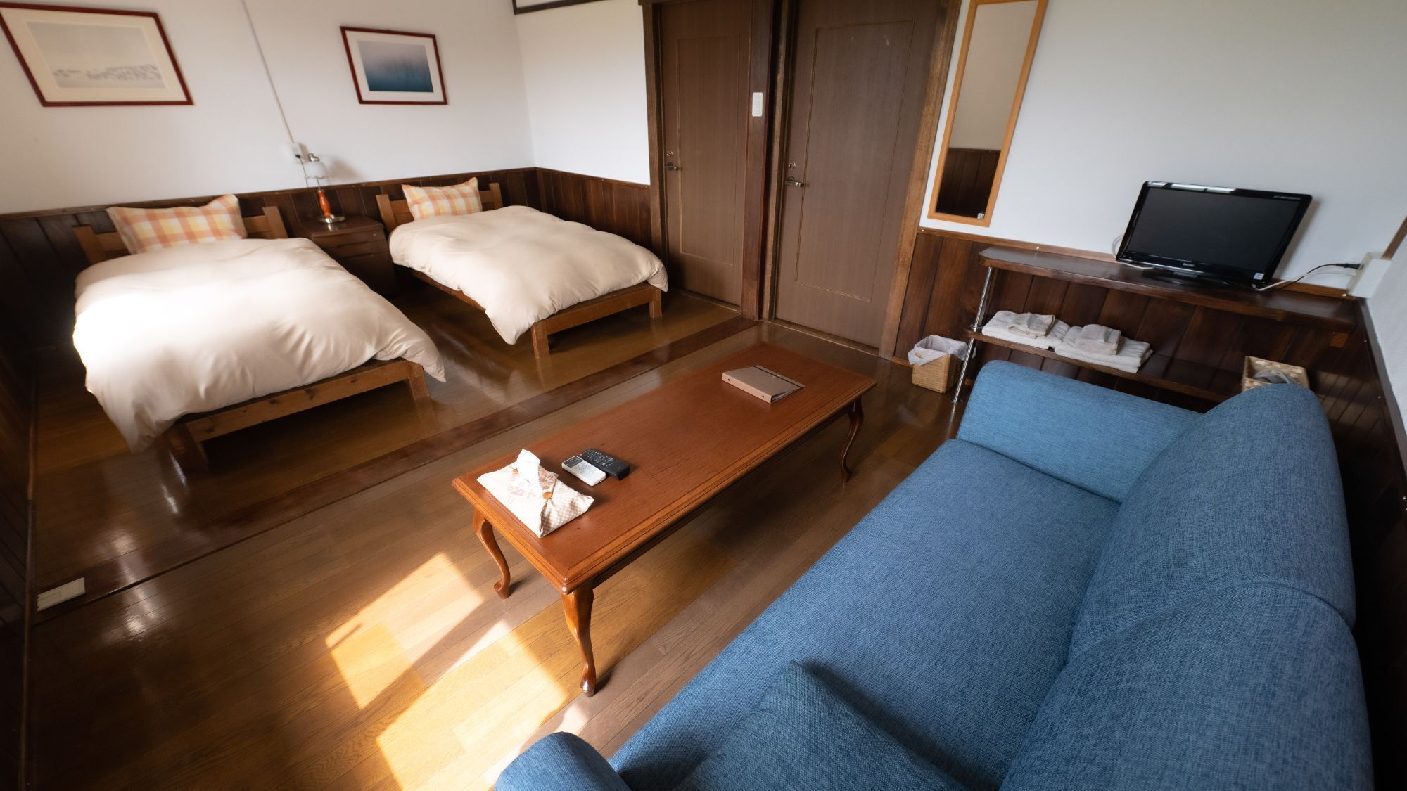 A hotel room with two beds, a sofa, a wooden coffee table, a television, and a wardrobe.