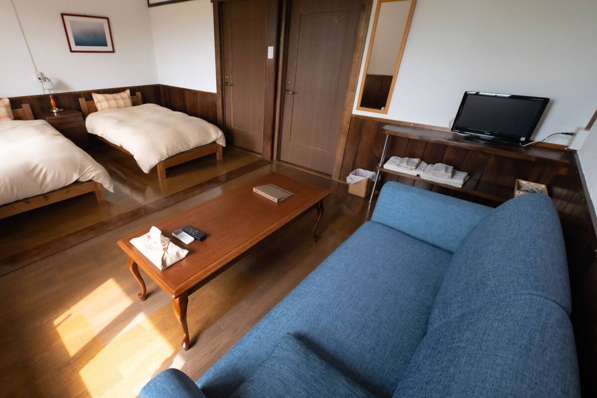 A hotel room with two beds, a sofa, a wooden coffee table, a television, and a wardrobe.