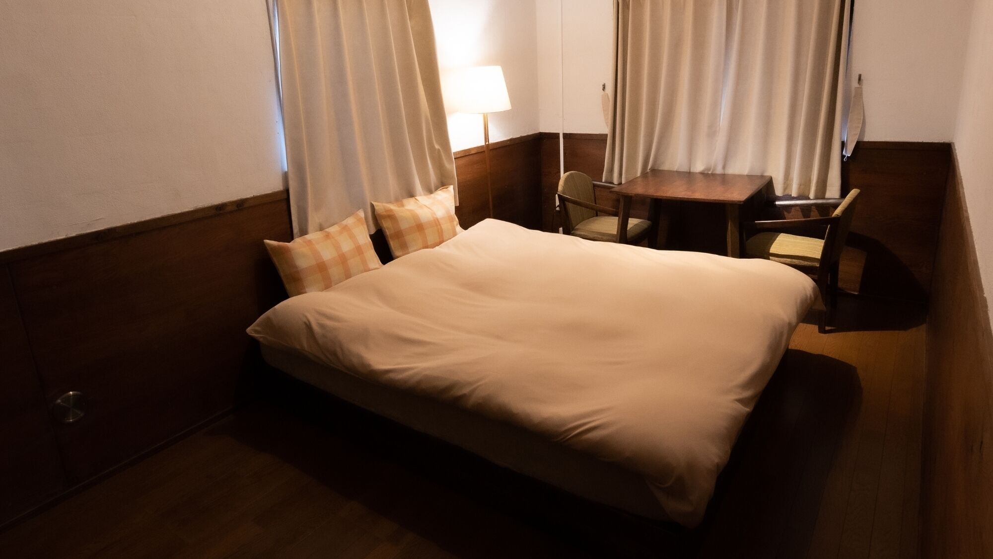 A hotel room with a bed, a small table, a chair, and curtains.