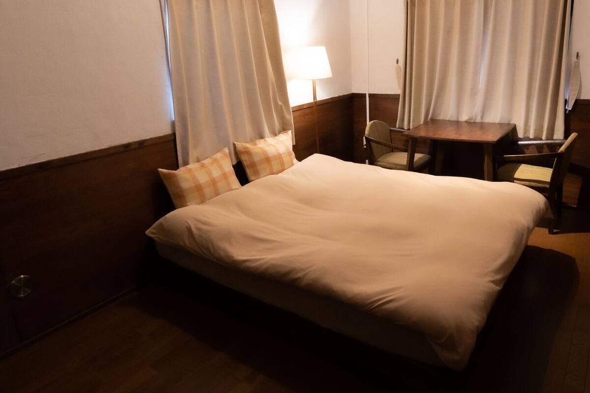 A hotel room with a bed, a small table, a chair, and curtains.