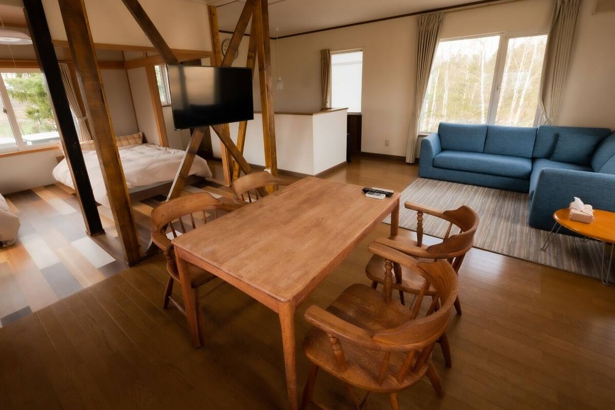 A cozy living room with a wooden dining table, blue sofa, and a TV mounted on a wooden beam.