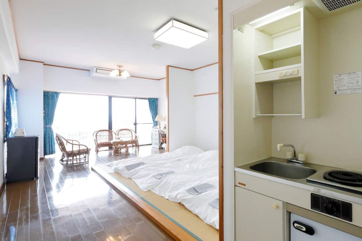 Habitación de hotel compacta con cama, kitchenette pequeña, comedor con sillas y vistas a través de una ventana.