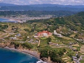 An aerial view of a coastal town with terraced fields, a prominent red building, and a beach. - Resort Hotel Umibe no Kajuen (Konan)