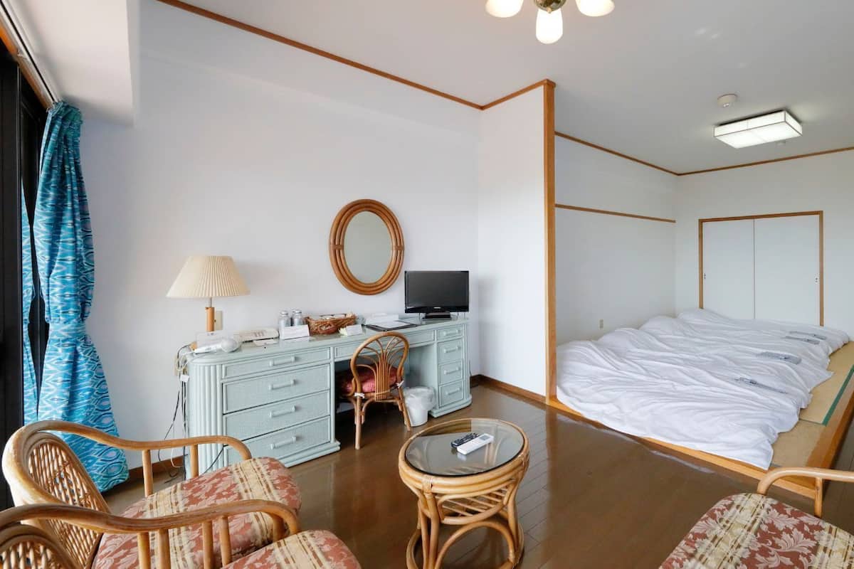 Habitación de hotel con cama, escritorio con computadora, silla, espejo redondo y televisión.
