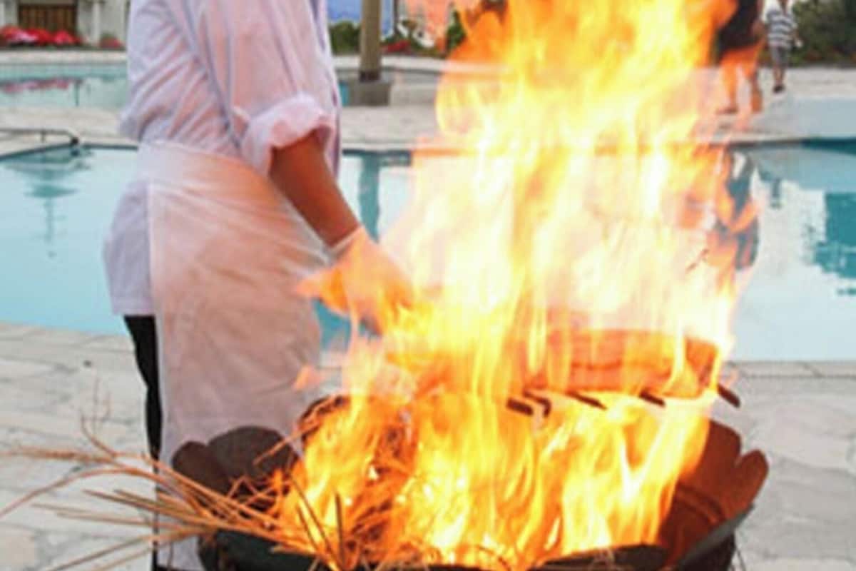 Un chef realiza un flambé con una gran llama en un ambiente junto a la piscina.