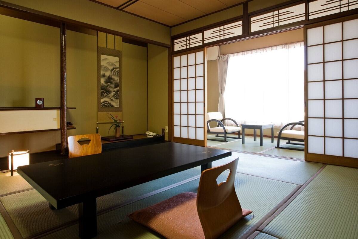 Um quarto japonês tradicional com tatames, uma mesa baixa, uma cadeira e portas deslizantes.