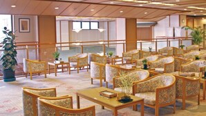 Un vestíbulo de hotel con filas de sillones estampados con motivos florales, una mesa de centro y plantas en macetas.
