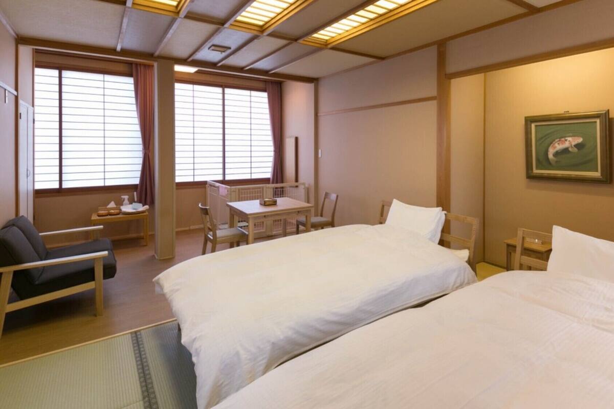 Quarto de hotel com duas camas, uma mesa, cadeiras e um quadro na parede.